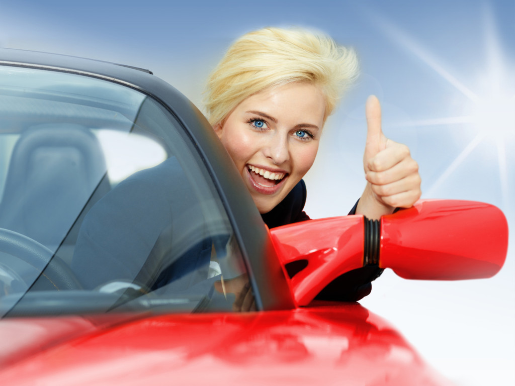 Beautiful 20s driving a red roadster and shows thumb up