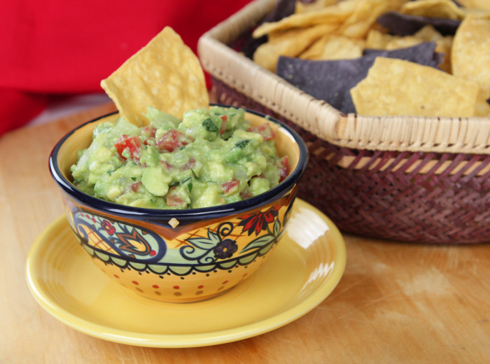 Bowl of guacamole dip with basket of tortilla chips.